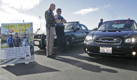 Kitsap County Patrol Chief Gary Simpson and Seattle Police officer John Bundy admire the Kitsap County undercover patrol car as they stand next to the “Slow Down or Pay Up” poster at King County International Airport Thursday.