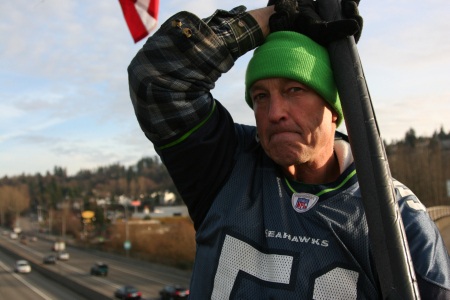 Navy veteran Fred Pepper is seen holding a flag pole on the I-405 Exit 7 overpass. Thousands see Pepper marching with the American flag most mornings.