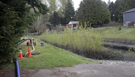 The water in a detention pond containing some sewage was being pumped out and into the sewer system on Northeast 10th Street and Duvall Avenue Tuesday in the Highlands. The water line is visible at the right; the dark color below the grass is typical and is not an indication of sewage.