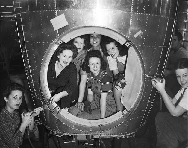 A group of  ‘Rosie the Riveters” pose for a photograph while working on an airplane during World War II.