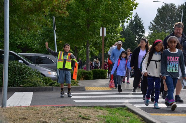 A student crossing guard blocks traffic as families file toward Kennydale Elementary School on the first day of school