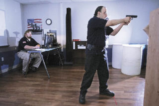 Kris Leonard of Seattle takes aim in a firearms training course at Kaplan College. He is aiming at a video screen that simulates various law enforcement situations. Leonard hopes to become a police officer. Instructor Ken Matelski of Greenwater supervises at left.