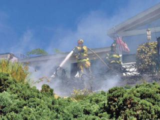 Firefighters with the Renton Fire and Emergency Services spray water on plants and a deck as they fought a fire Friday afternoon on Lake Washington Boulevard in Kennydale. The fire’s cause is still under investigation.