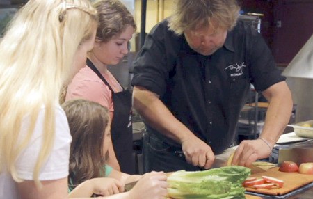 Famed Seattle Chef Tom Douglas demonstrates the fine art of preparing vegetables for a trout dish for Carolyn Ossorio and her daughters Amelia and Sophie.