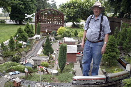 Jim Arlint towers above the garden railroad he’s built on a 75-foot long and 24-foot wide L-shaped platform in his yard. Aside from the people