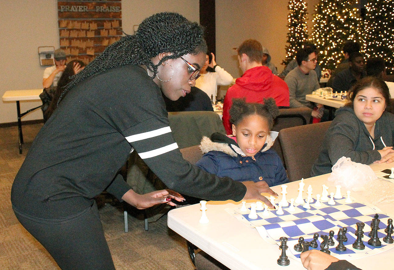 Phiona Mutesi, an international chess champion from Uganda who was depicted in a movie “Queen of Katwe,” helps 10-year-old Thalia Smith arrange the chess board as 13-year-old Samantha Valenzuela looks on during a Chess with the Superintendent session Wednesday at Family Life Community Church. The youth, most of whom are students in Federal Way, received a basic lesson from Superintendent Tammy Campbell, while Mutesi walked around offering pointers to students. The students left with a chess board of their own. JESSICA KELLER, the Mirror