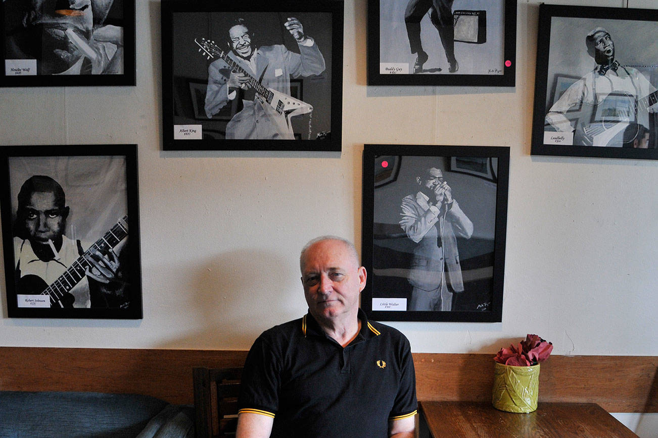 Mick Flynn sits underneath his “Blues Greats” acrylic series at Liberty Cafe. Photo by Leah Abraham
