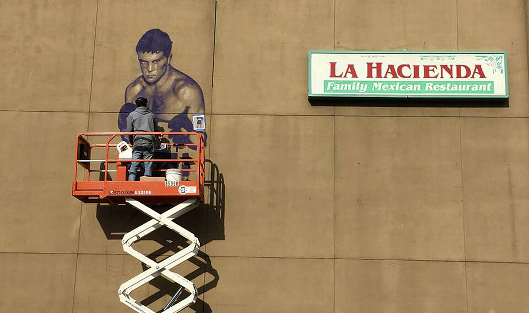Courtesy photo                                Artist Will Schlough works on a mural of hometown hero Boone “Boom Boom” Kirkman. The mural will be celebrated Wednesday, Nov. 21 from 5 to 7 p.m. along the wall of La Hacienda Santa Fe on South 3rd Street.