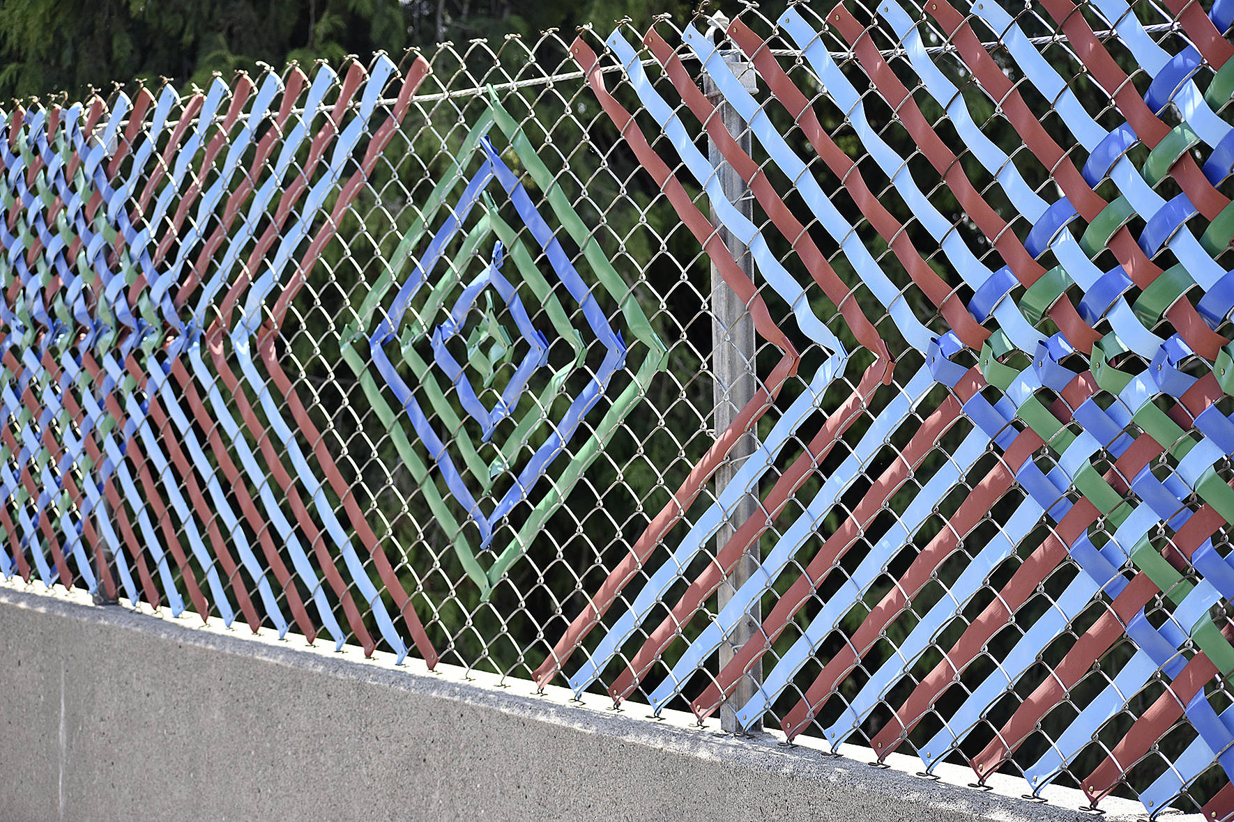 Photo by Haley Ausbun. The fence now has woven with colorful privacy tape, plaques containing six languages and over 100 symbols that were created by students and residents in the Sunset neighborhood.