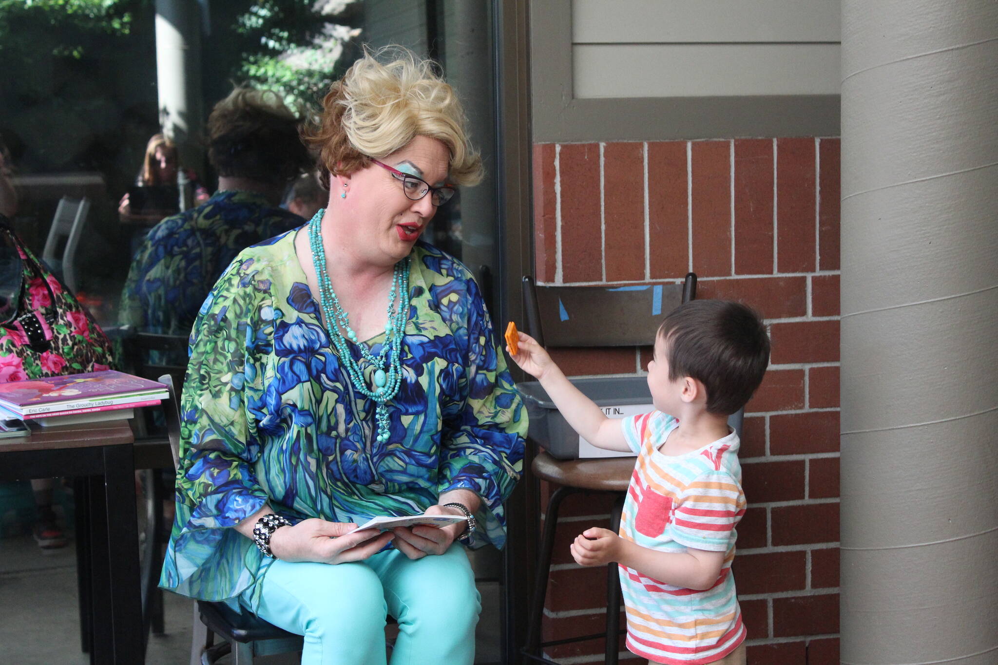 A boy offers Sylvia a cracker during Drag Queen Storytime. Photo by Bailey Jo Josie/Sound Publishing.