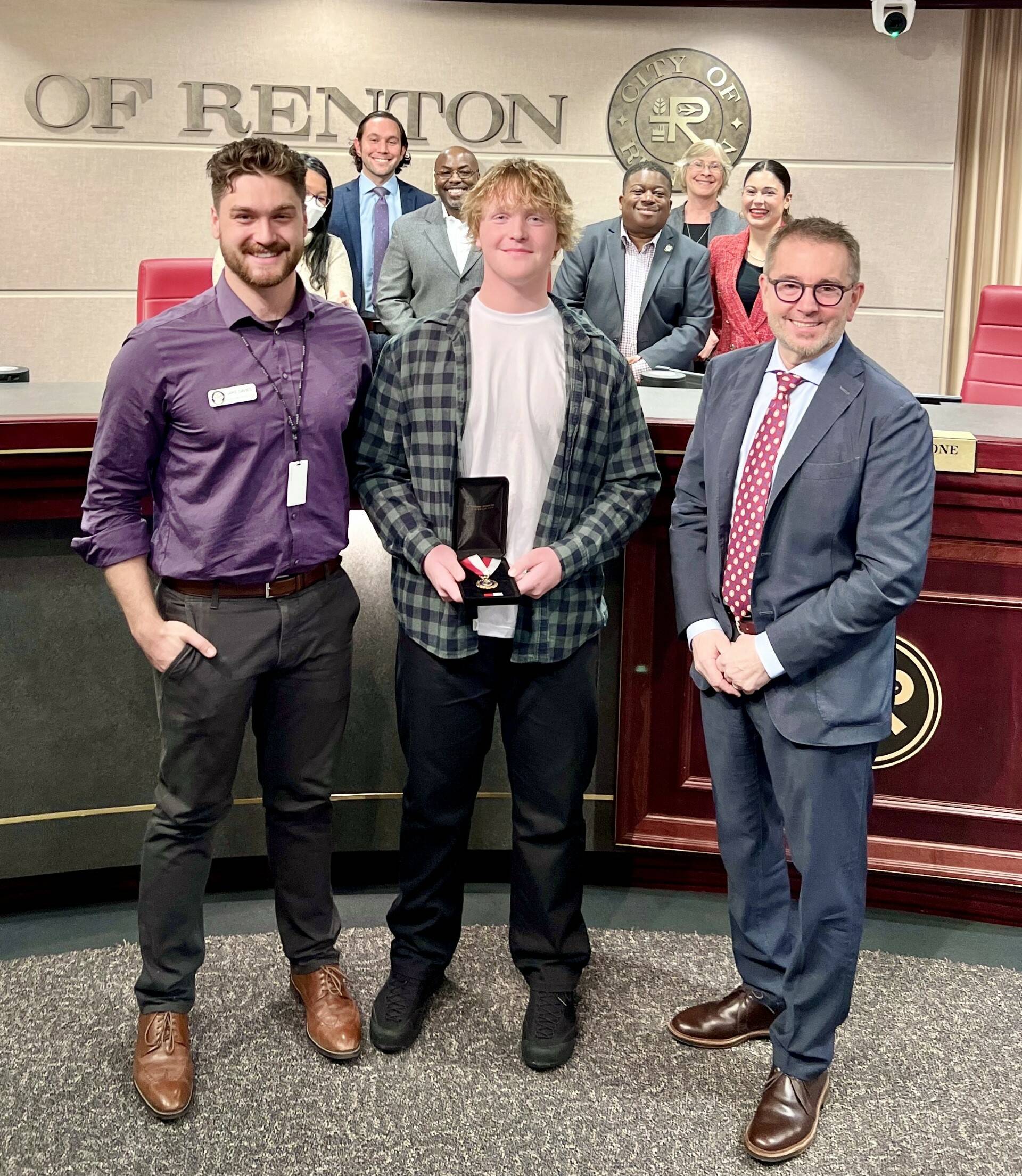 Braeden McSweeney, center, holds his Renton Police Department Life Saving Medal, standing with his boss and coach, Jake Davies, Mayor Pavone and the Renton City Council in the background. Courtesy photo.