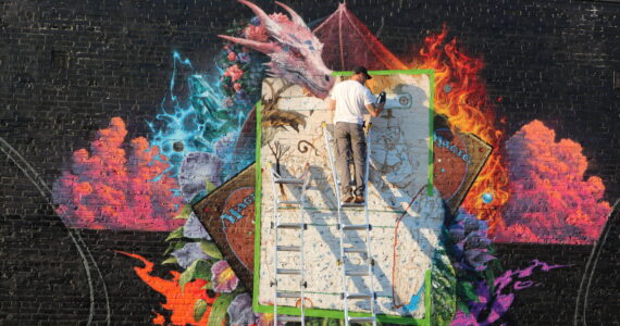 Spray paint mural artist Jeff Weirdo (@weirdocult on Instagram) works on the latest downtown mural on Williams Avenue, which is in partnership with Wizards of the Coast, a Renton-based game company famous for Dungeons & Dragons and Magic: The Gathering. Photo by Bailey Jo Josie/Sound Publishing