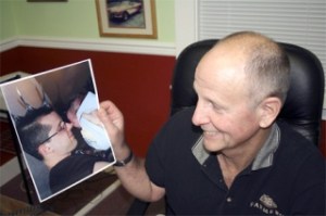 Oscar Myre the Third holds a photograph of son Oscar Myre the Fourth holding his son Oscar Myre the Fifth on Wednesday at his office in Renton.  The senior Myre missed watching the  Evening Magazine show Wednesday night about the family because he was at a hot-rod class at Renton Technical College.