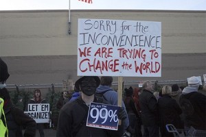 An Occupy Renton protester outside the Walmart store Friday afternoon on Rainier Avenue makes his point in a black mask.