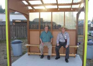 Maplewood Neighborhood Association President Bob Johnson and Vice President Dennis Wood sit on the bench that was added to their new bus shelter by an unknown builder.