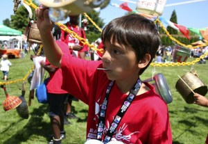 Nahiyaw Northwind bangs on various 'instruments' hanging beneath a tent at Renton River Days.