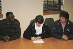 Brandon Schaefer signs his letter of intent to play soccer at Evergreen State College. Renton High School athletic director Charles James (left) and Brandon’s father Duane Schaefer watch.