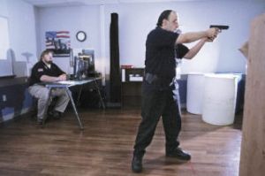 Kris Leonard of Seattle takes aim in a firearms training course at Kaplan College. He is aiming at a video screen that simulates various law enforcement situations. Leonard hopes to become a police officer. Instructor Ken Matelski of Greenwater supervises at left.