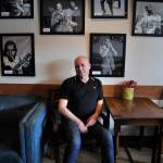 Mick Flynn sits underneath his Blues Greats acrylic series at Liberty Cafe. Photo by Leah Abraham