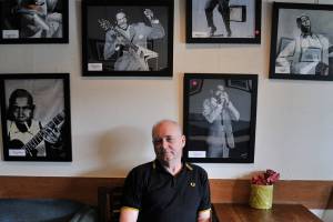 Mick Flynn sits underneath his Blues Greats acrylic series at Liberty Cafe. Photo by Leah Abraham