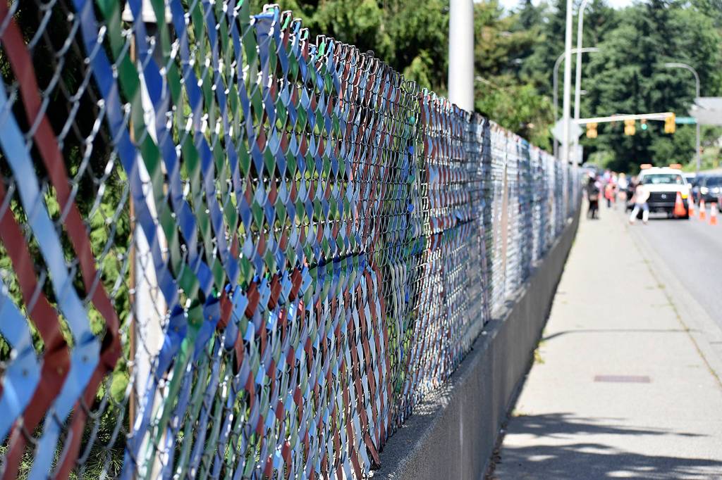 Photo by Haley Ausbun. The fence now has woven with colorful privacy tape, plaques containing six languages and over 100 symbols that were created by students and residents in the Sunset neighborhood.