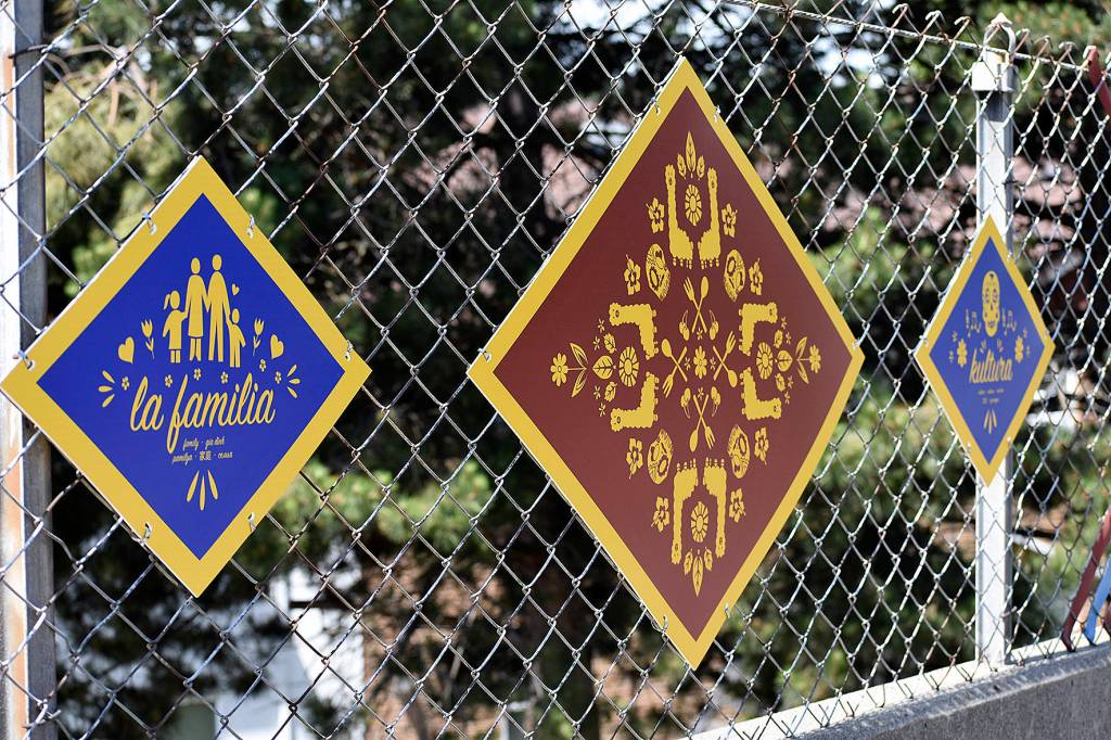 Photo by Haley Ausbun. The fence now has woven with colorful privacy tape, plaques containing six languages and over 100 symbols that were created by students and residents in the Sunset neighborhood.
