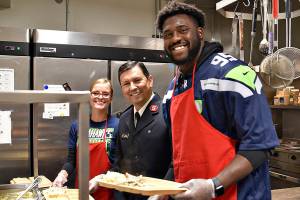 Photo by Danny Rodgers for The Salvation Army.                                Seattle Seahawks Defensive End L.J. Collier volunteers at The Salvation Army community meal on Wednesday, Nov. 26, helping serve a traditional Thanksgiving meal. The Salvation Army serves a free meal to the public, Monday through Thursday, 5:15 to 6:30 p.m. Also pictured are Captain Isaias Braga, director of The Salvation Army in Renton, and Larissa Braga, volunteer.
