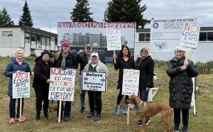 The Logan 6 protesters posed in front of signs detailing the new development planned for the lot between N. 3rd Street and 4th Street. Photo by Drew Dotson/Renton Reporter