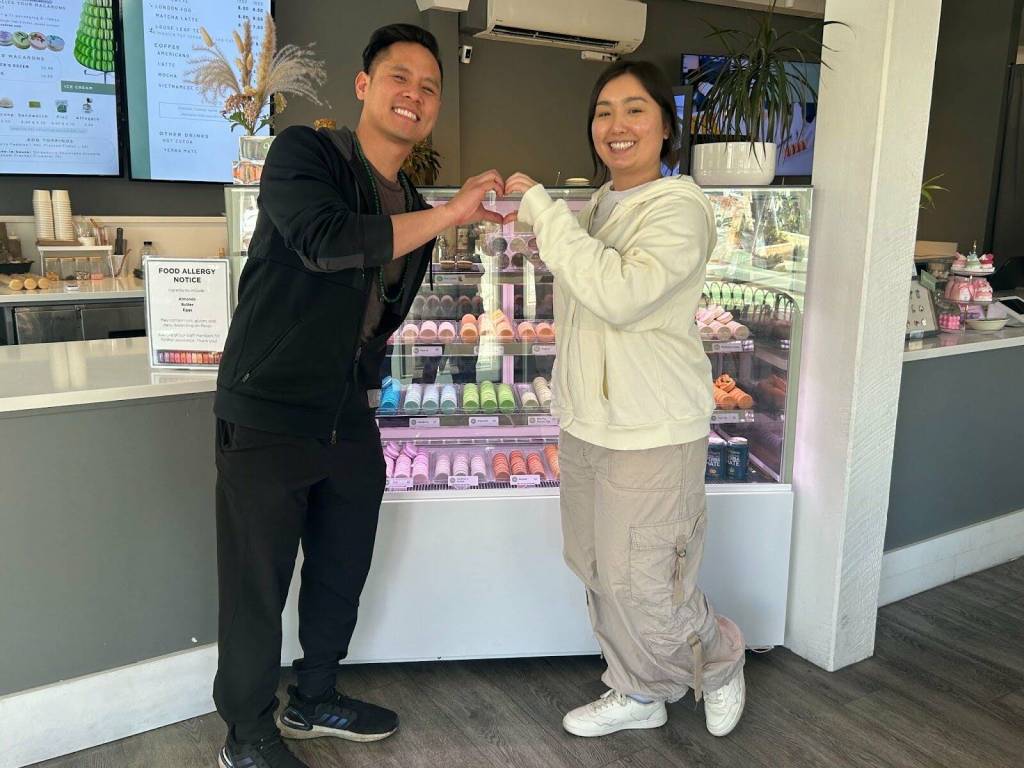 Picture of business owner Michael Huynh and employee Jemmy making a heart sign in front of their flavorful display of macarons. Photo by Janiyah Gibson/The Reporter